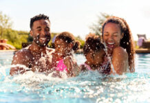 Family On Summer Holiday With Two Girls Being Held In Swimming Pool By Parents And Splashing