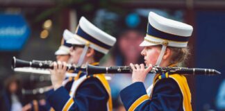 Stock photo of teens playing instruments in a marching band. They are wearing matching navy blue and gold uniforms with marching band hats.