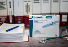 Stock photo of a box that is labeled "Ozempic" in blue text on a table in front of different medical books.