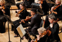 Photo of a Black man with short dark hair playing the violin on stage with an orchestra.