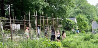 Photo of people inside a wooden stick structure in a community garden. Greenery surrounds them.