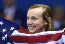 Katie Ledecky: The Most Decorated Female American Olympian of All Time Photo of a woman smiling. Only her head is visible from behind an American flag she's holding.