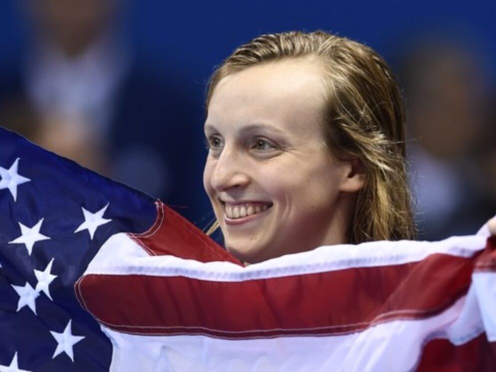 Photo of a woman smiling. Only her head is visible from behind an American flag she's holding.
