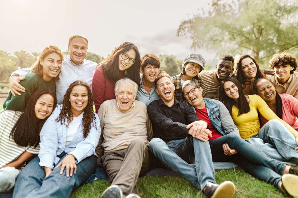 Stock photo of more than a dozen adults, some of them older adults, sitting outside and laughing together.
