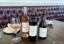 Wining and Dining at The Farmhouse Bistro at The Crossvines Photo of a glass with a small amount of light orange-colored wine next to three wine bottles on a restaurant table.