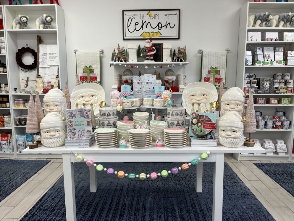 Photo of the interior of a boutique that sells home decor and seasonal gifts. There is a string of pastel-colored beads decorating the white table and stacks of Santa-themed plates and dishes.