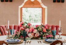 Photo of the interior of a large grand ballroom with bouquets of pink flowers on the table set for dinner.