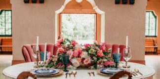 Photo of the interior of a large grand ballroom with bouquets of pink flowers on the table set for dinner.