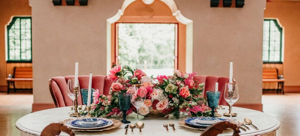 Photo of the interior of a large grand ballroom with bouquets of pink flowers on the table set for dinner.