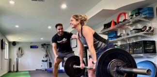 Photo of a woman deadlifting a barbell in a gym with a male trainer coaching her in the background.
