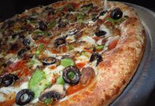 Cuginis Restaurant and Bar Wins Eight Readers’ Choice Awards Close-up of a pizza topped with green peppers and black olives.