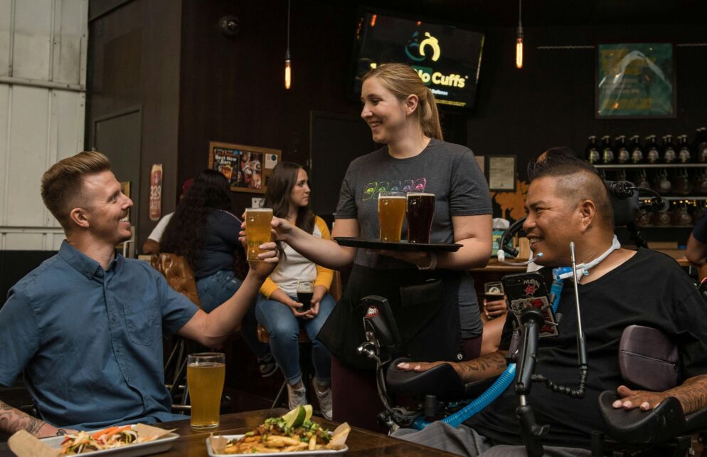 Stock photo of two men receiving glasses of beer from a waitress at a pub-style restaurant.