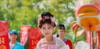 Stock photo of a Chinese dancer dressed in a traditional pink floral dress and a pink floral headband. She is dancing at a street festival with other Chinese dancers.