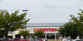 Stock photo of a grocery store building with large red italicized letters that read "Shoppers" on the front.