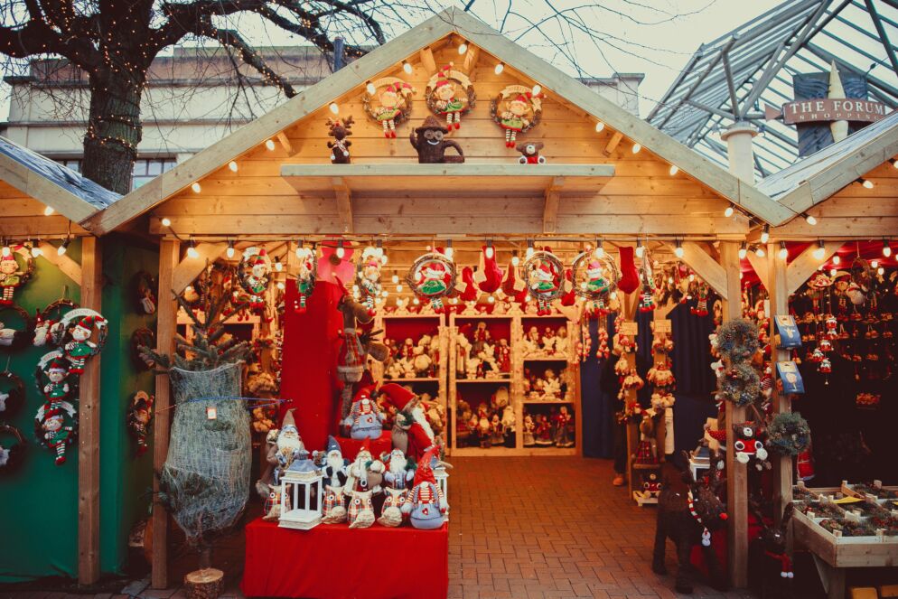 Photo of a holiday market in a wooden house-like structure with shelves of plush animals, ornaments and Christmas-themed decor.