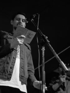 Man reading poetry from a book at an open mic